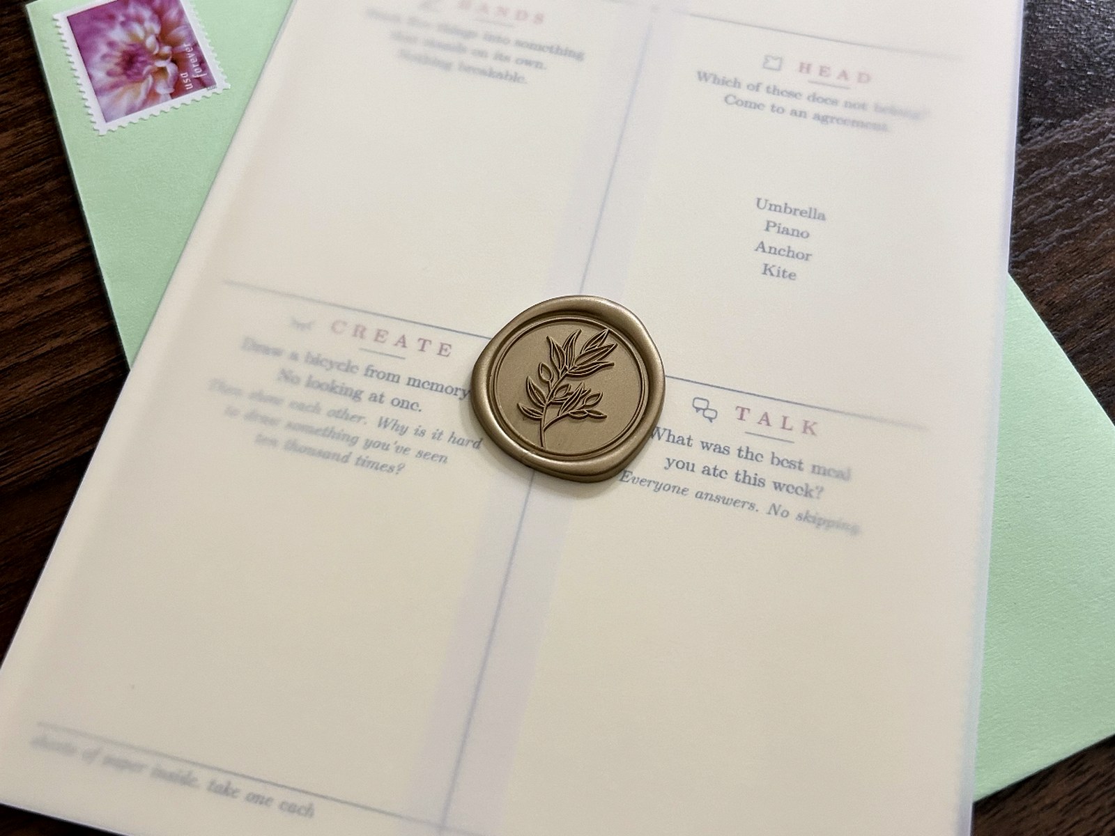 A cream card wrapped in vellum and closed with a gold wax seal, resting on a mint envelope with a stamp.